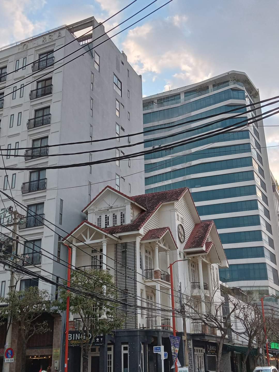 A traditional house with tall white pillars and a red roof sits nestled among two tall modern buildings in Da Nang, Vietnam