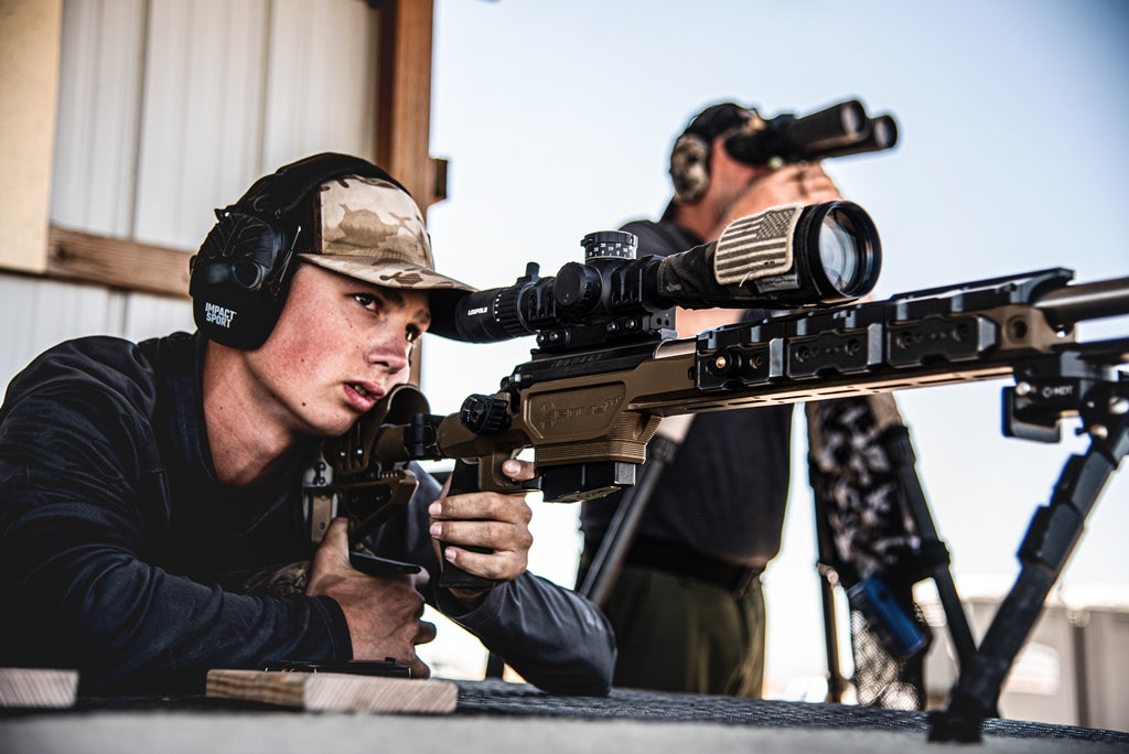Properly fitted precision rifle shooter - Executing long-range shots with a spotter on glass.