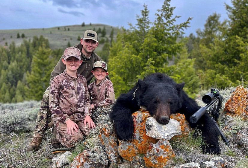 Happy dad and kids posing proudly with their harvested bear, showcasing their successful hunting adventure with their youth hunting rifle