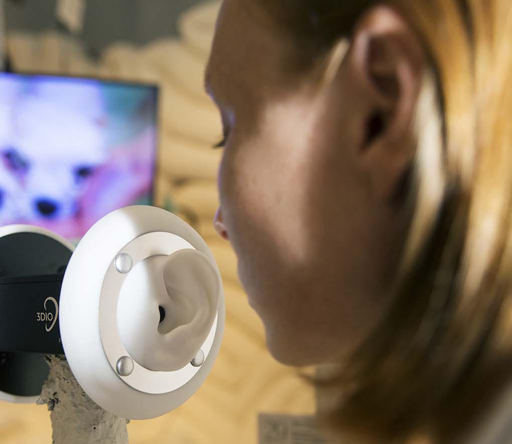 A woman is speaking into the prosthetic ear of a 3Dio binaural microphone.