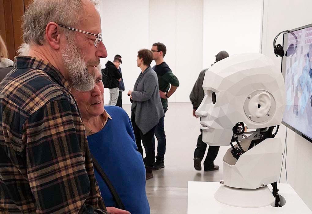 Image of an older couple in a museum looking at an animatronic human-shaped head.
