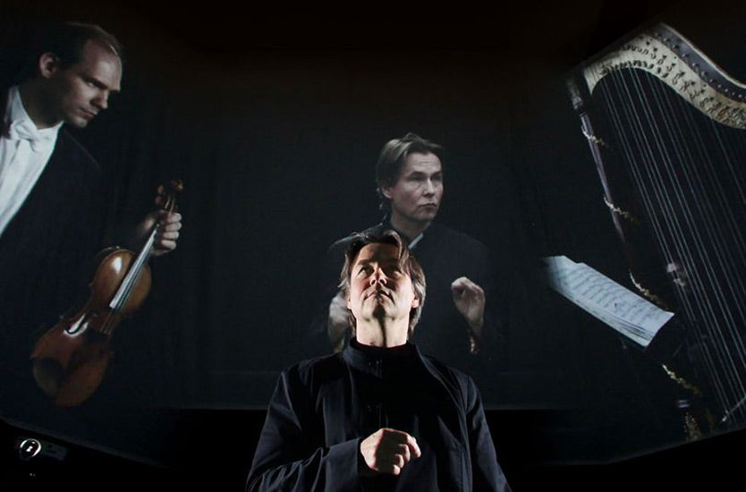 Image of a maestro standing in front of a large projection of musicians.