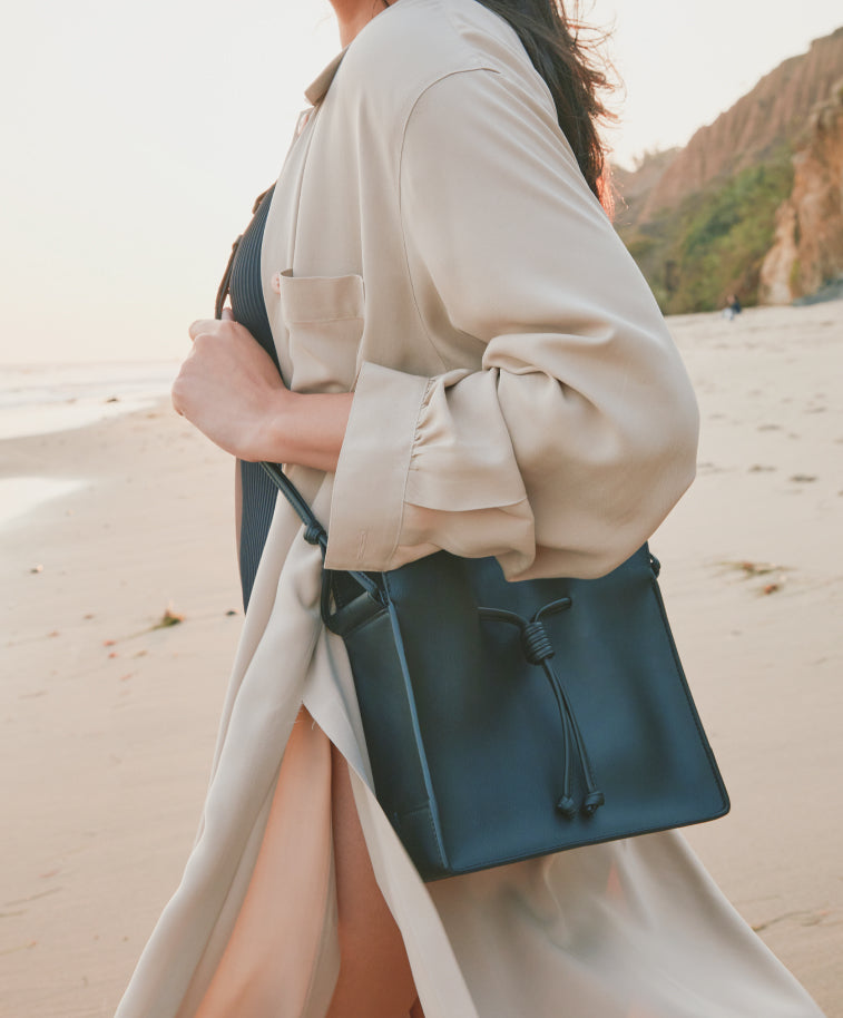 Woman in beige coat carrying a medium shopper over her shoulder standing  on the beach