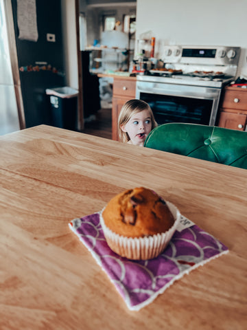 little girl with tongue out looking at muffin