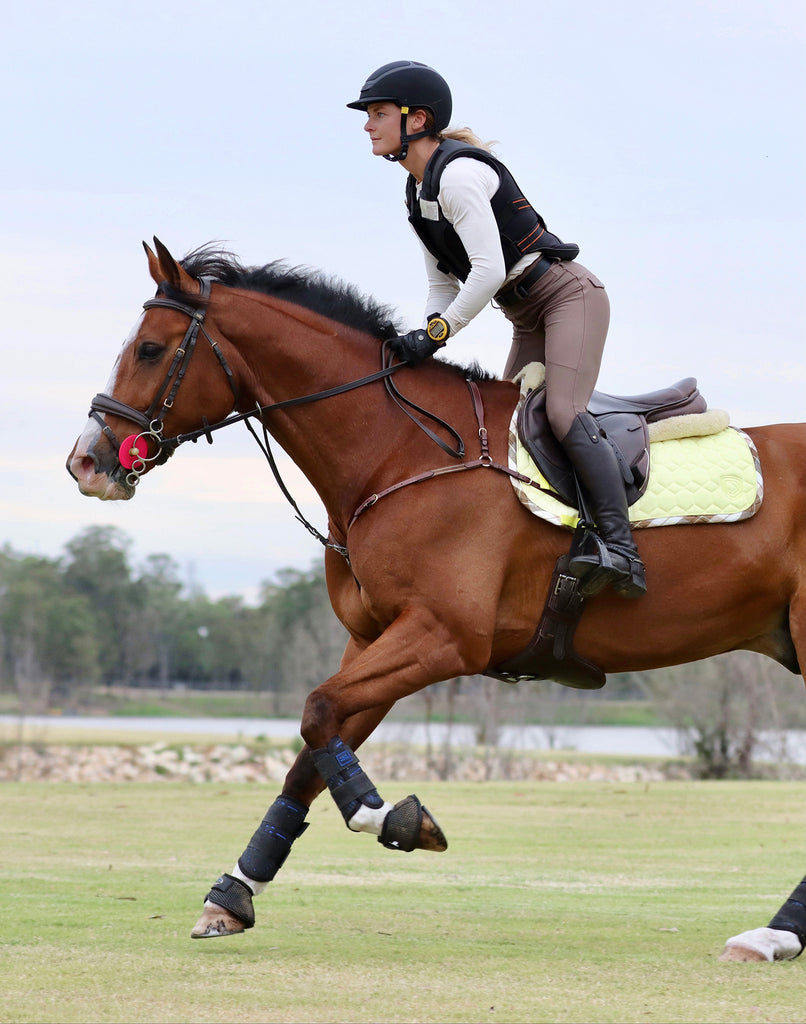 girl riding in a field on a bay horse with citrus coloured saddle pad