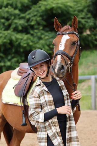 girl smiling with her chestnut horse wearing a citrus flannel top and helmet