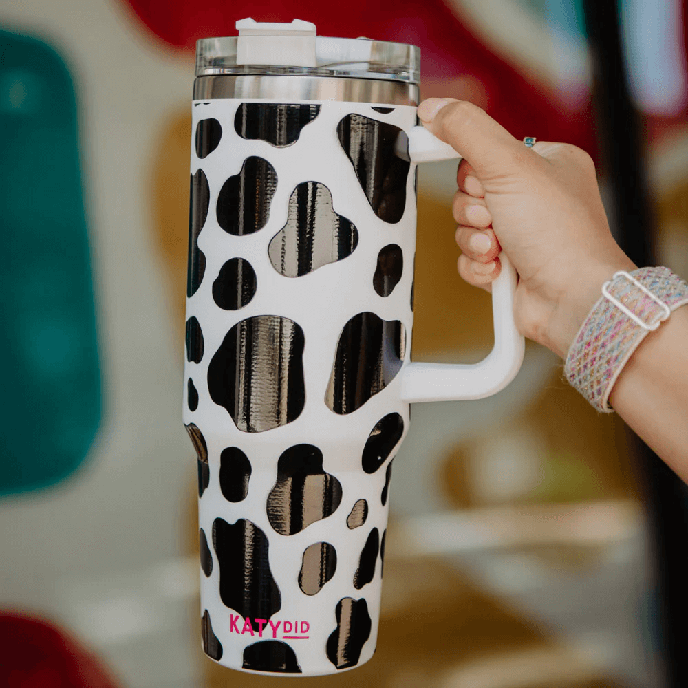 A woman holding a black and white cow print stainless steel tumbler cup
