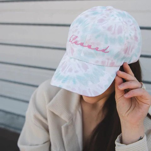 woman in a jacket and tie-dye blessed baseball cap