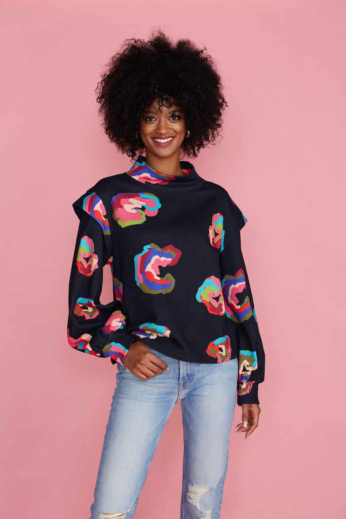 Woman in black mock neck sweatshirt printed with colorful leopard spots