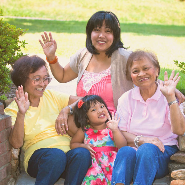 Four generations of Filipino women wave to the camera with joyful smiles.