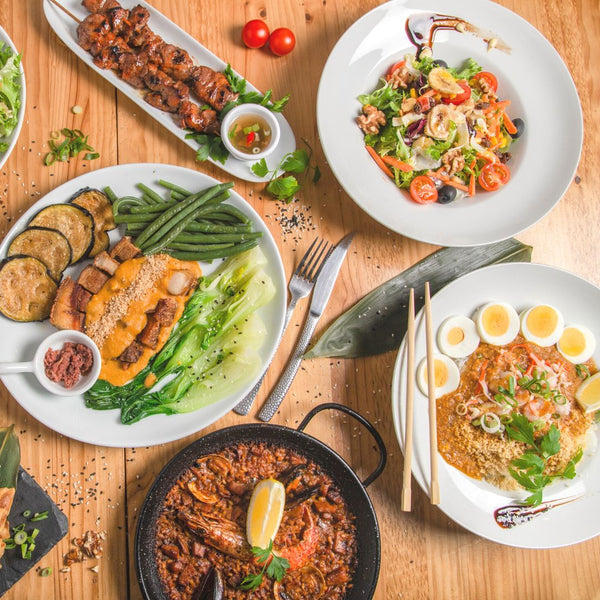 A feast of Filipino dishes spread out on a table featuring Pinoy barbecue, paella, kare-kare, pansit, and more.