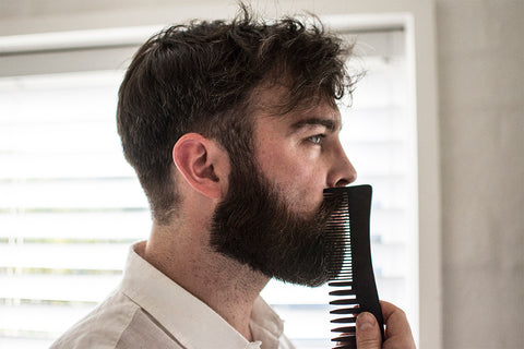 man combing beard in bathroom mirror