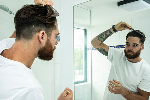 man combing hair in bathroom mirror