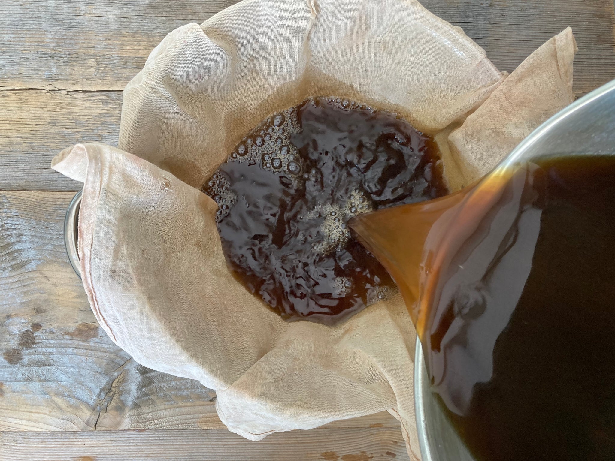 Straining the saucepan of steeped acorns through a sieve lined with muslin cloth