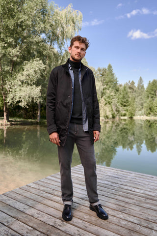 Tall man standing on dock with lake in background. He is wearing dark jeans and a black jacket