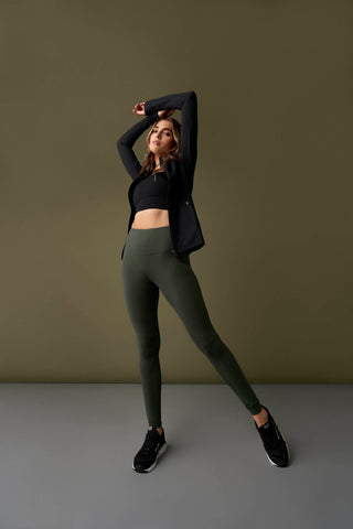 Woman standing with arms stretched above head wearing high rise leggings, sports bra and athletic zip jacket