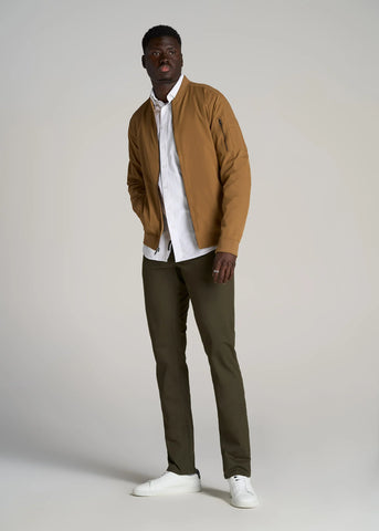 Man standing wearing tall tapered fit chinos with light colored button shirt and sand coloured bomber jacket