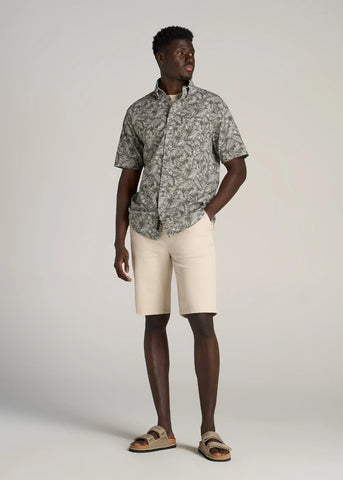 Man with hand in pocket wearing light beige shorts and floral short sleeve button shirt