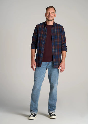 man standing wearing straight leg, light colored jeans with plaid button shirt open over tee