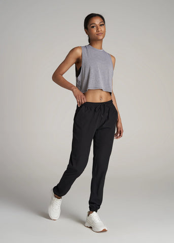 Woman standing with hand in pant pocket wearing black joggers and loose cropped gray tank top