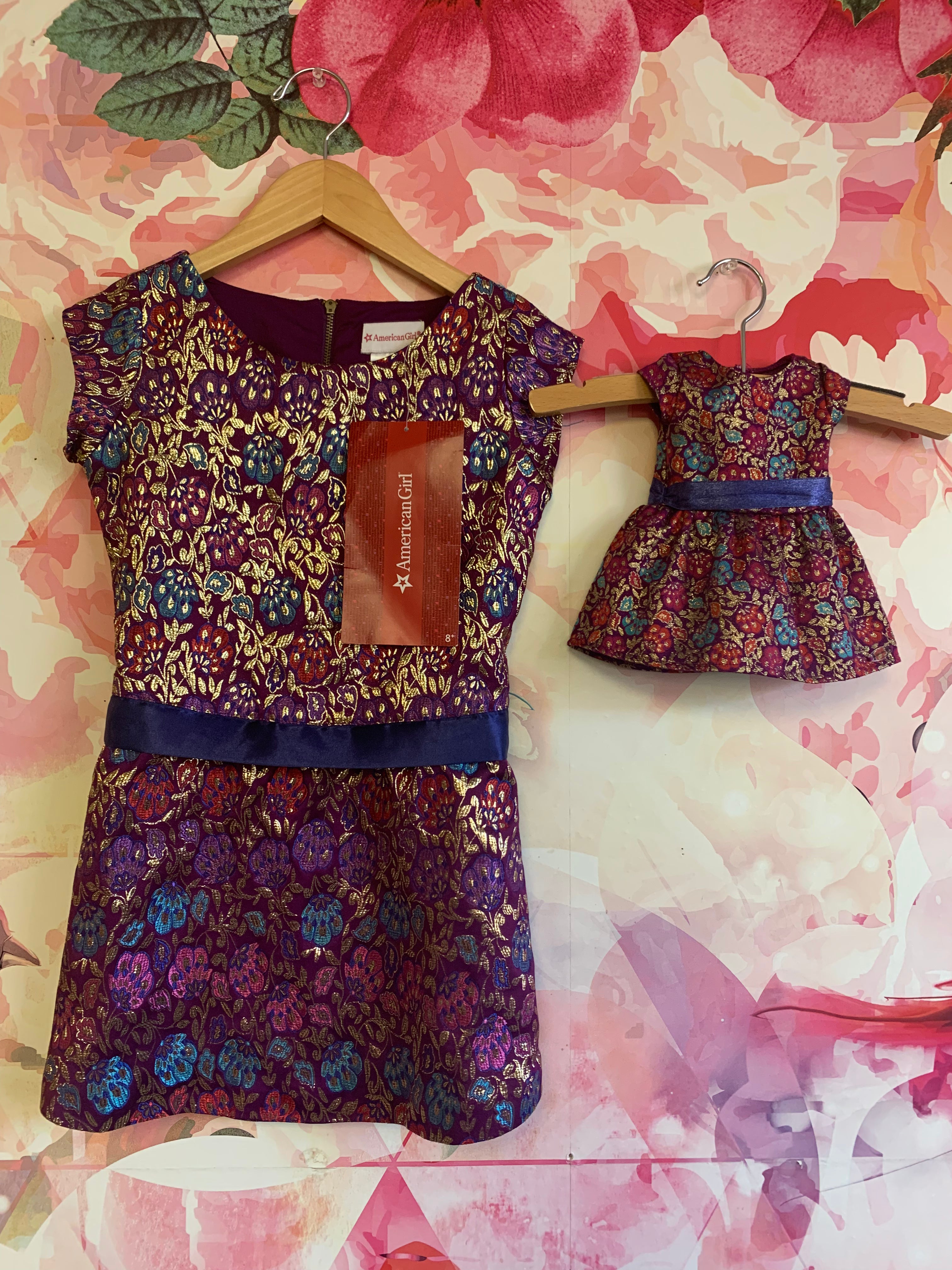 American Girl purple short sleeve dress with fuschia, red, blue, gold flowers & blue waist sash. Zipper back. Size 6. Includes Matching dress for doll. NEW WITH TAGS