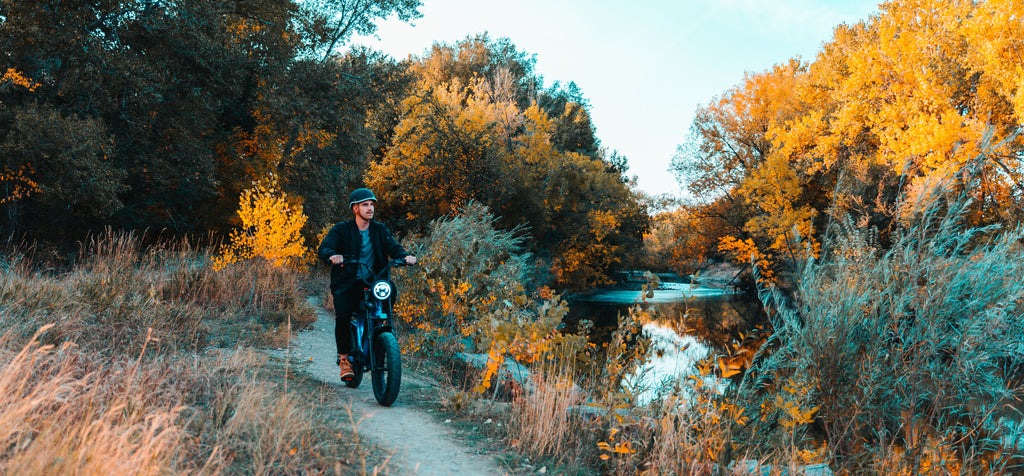 Man riding Juiced Bikes HyperScorpion through wooded area next to a stream during the fall