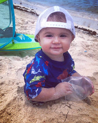 baby boy half buried in sand at the beach wearing a rash guard