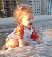 baby girl playing in the waves at the beach in a swim diaper and rashguard