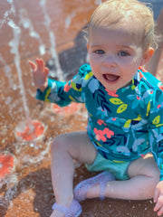 happy baby sitting at a splash pad wearing a BBLittles swim diaper