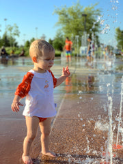 baby standing in a splash pad wearing a Beau and Belle Littles swim shirt and swim diaper