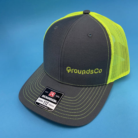 embroidered trucker hat with gray front and bill and neon yellow mesh with grounds co logo on left panel