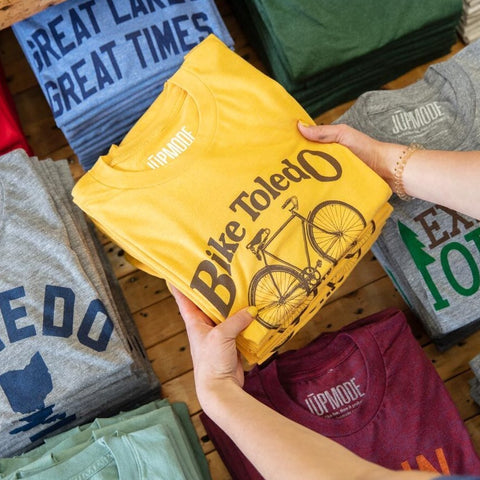 folded bike toledo shirt being laid on a table with shirts