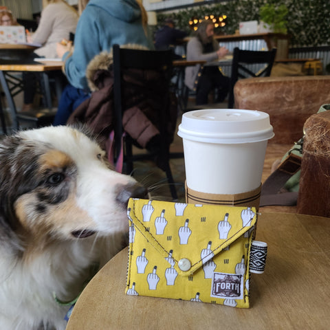 Dog sniffing a coffee next to a yellow avail middle finger wallet