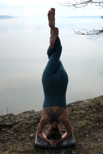 Yoga teacher Ranja Weiss is doing a headstand at the shore of a lake wearing a yoga outfit from Mandala.