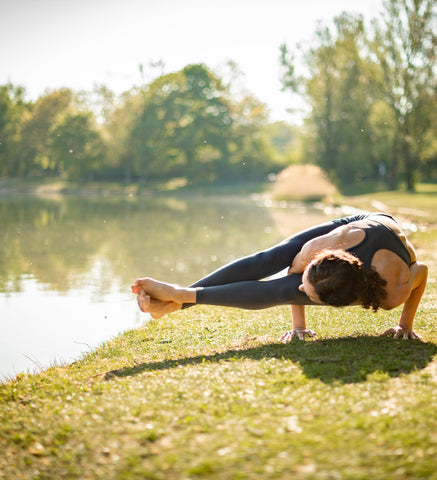 Yogalehrerin Anja Weiß macht eine Krähen-Variante (Yoga Asana) im Park und trägt ein Outfit von Mandala Fashion