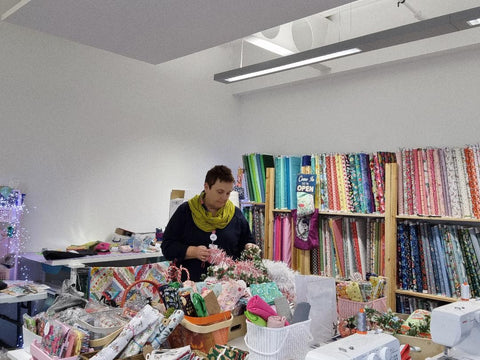Ellie, a middle aged and rather chubby white woman is sorting out bundles of fabric the her studio