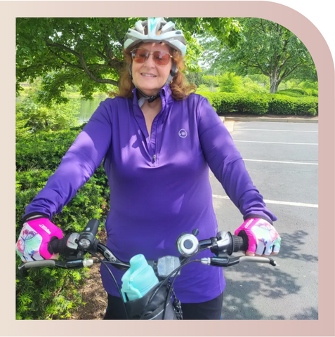 A customer riding a bike while wearing a purple Spark Half-Zip by Veil Garments, a modest activewear sweatshirt.