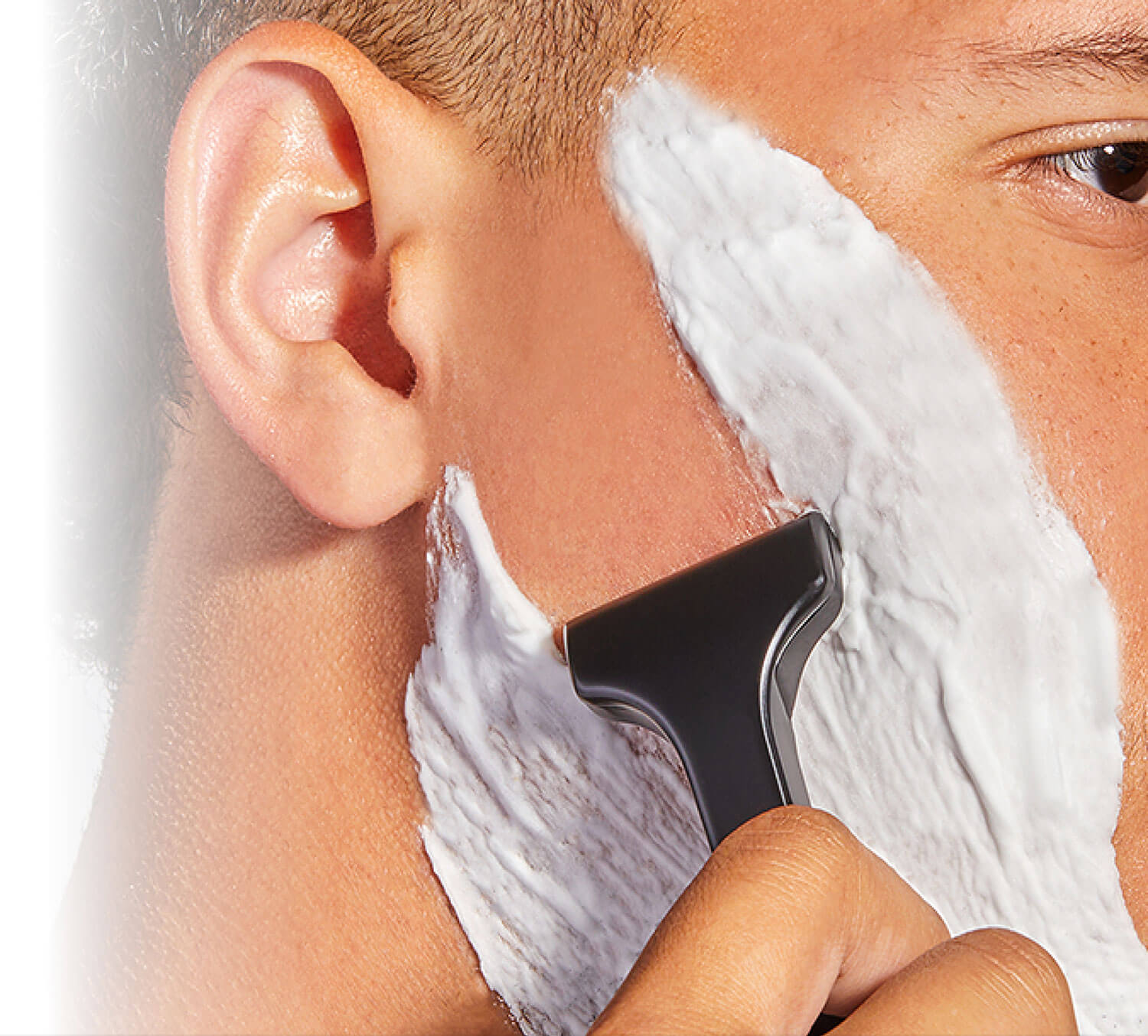 Close-up of a person shaving their face with a razor and shaving cream.