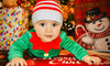 Baby in festive elf outfit underneath Christmas Tree 
