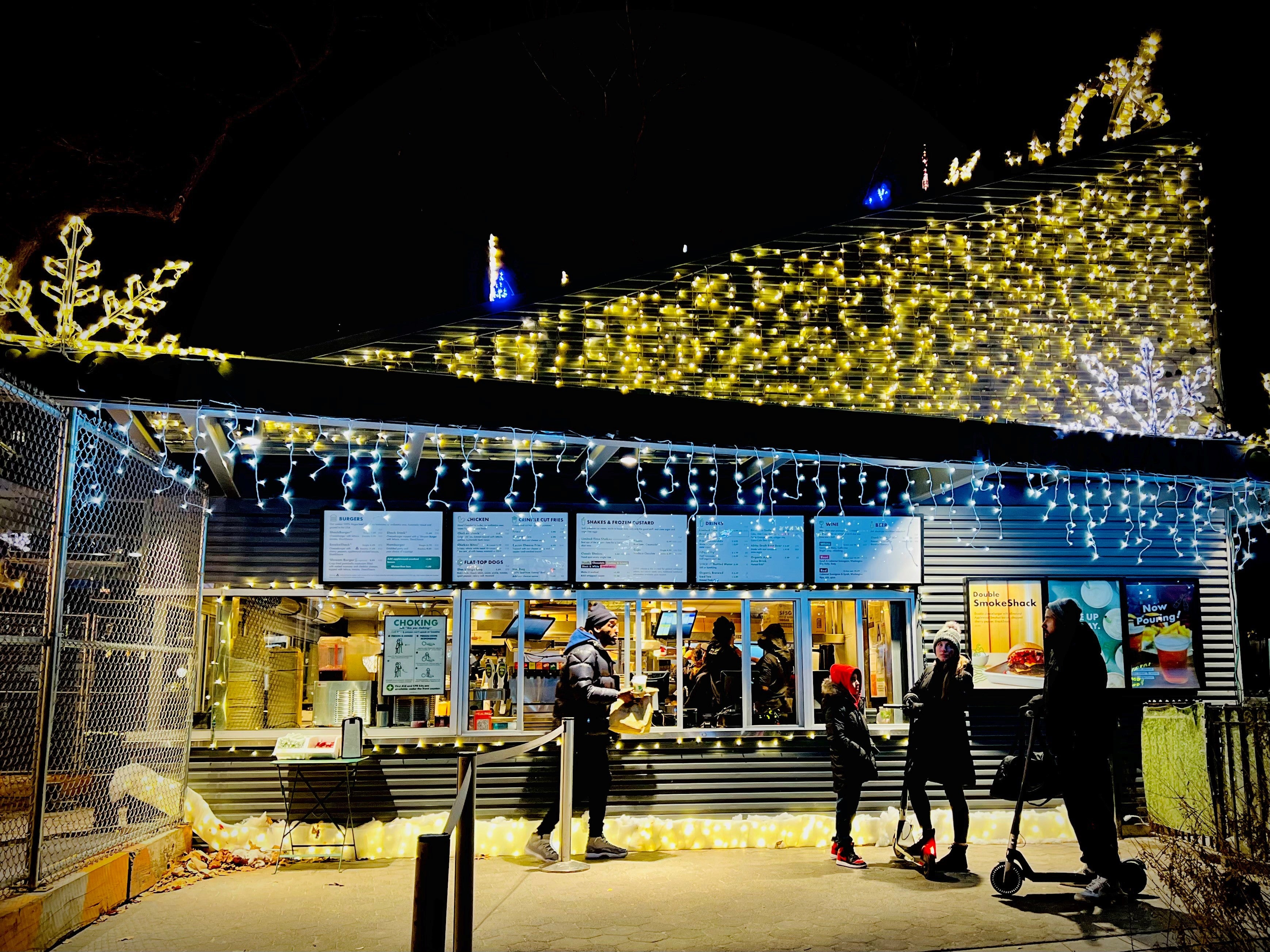 NYC christmas shake shack holiday decorations side of Madison Square Park burger kiosk with icicle lights and mix of warm white and cool white lights