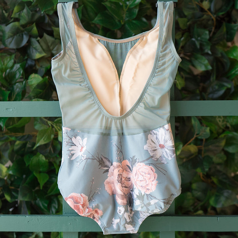 Back view of sleeveless dancewear leotard with a light blue bottom base and a flower print in hues of pink and white. The top half is in a teal-like blue mesh that has a middle/low cut back.