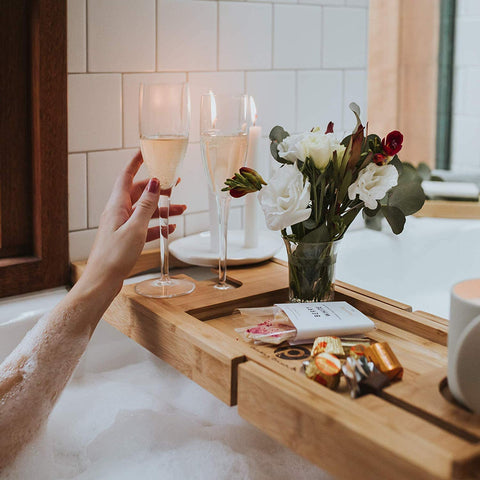 bathtub caddy, bamboo bath caddy tray, bathtub tray, wine glass, bathtub, flower vase, woman's hand