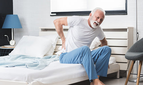 Elderly man sitting on a bed holding back in pain