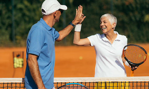 Two people holding tennis rackets high-fiving over the net