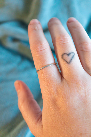 Image of thin silver stacking ring on pointer finger of woman's hand