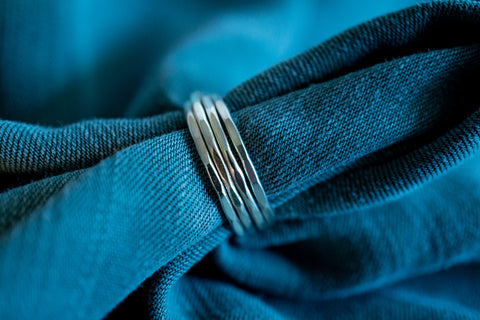 Image of four thin silver rings with hammered texture on blue fabric