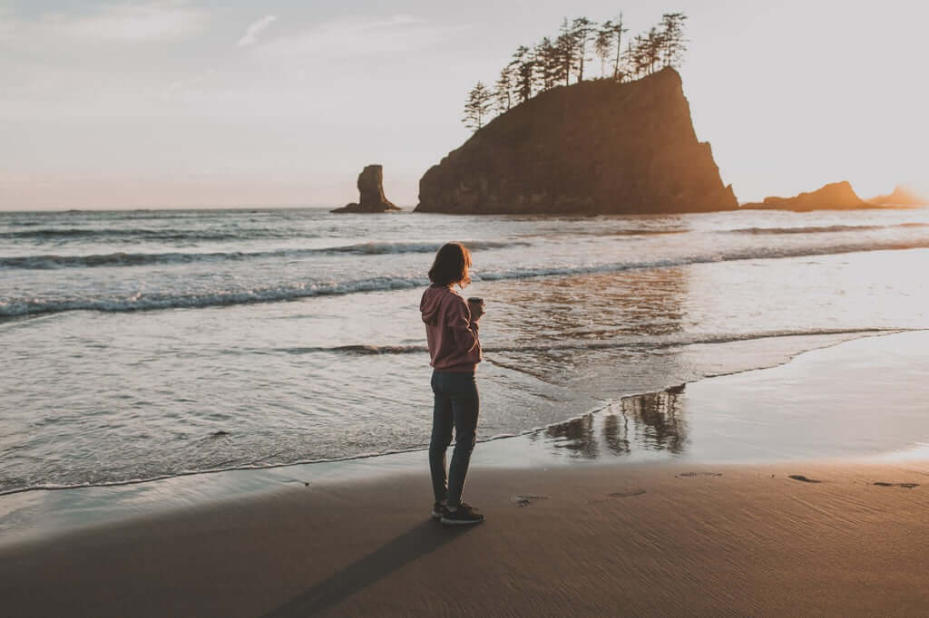 A woman stand alone on the beach drinking a nice beverage