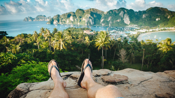 Punto di vista di un ragazzo in infradito e con le gambe davanti a sé, che guarda dall'alto una bellissima spiaggia hawaiana.