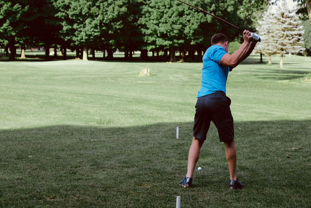 Man playing golf wearing a light blue polo shirt and dark grey shorts.