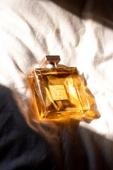 golden bottle of perfume on a white bed sheet